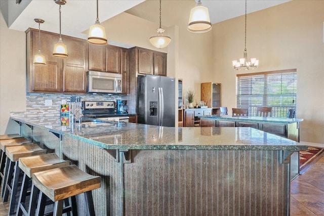kitchen featuring stainless steel appliances, decorative backsplash, a peninsula, a chandelier, and a breakfast bar area