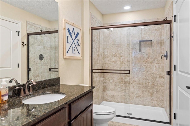 full bath featuring toilet, vanity, a textured ceiling, and a stall shower