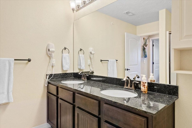 full bathroom with visible vents, a sink, double vanity, and a textured ceiling