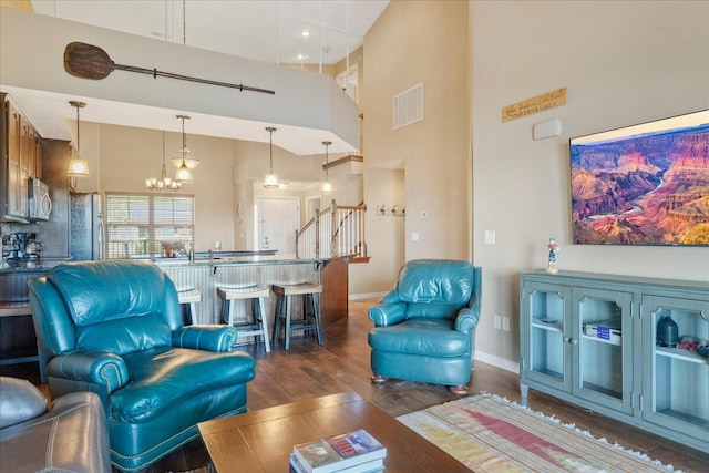 living room with a high ceiling, dark wood-style floors, an inviting chandelier, visible vents, and baseboards