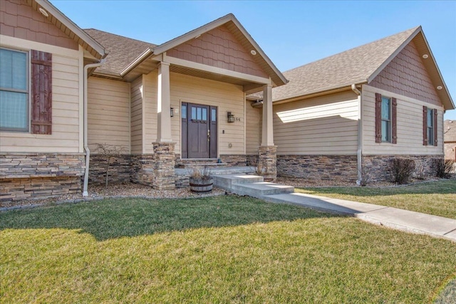 view of exterior entry with stone siding, a lawn, and roof with shingles