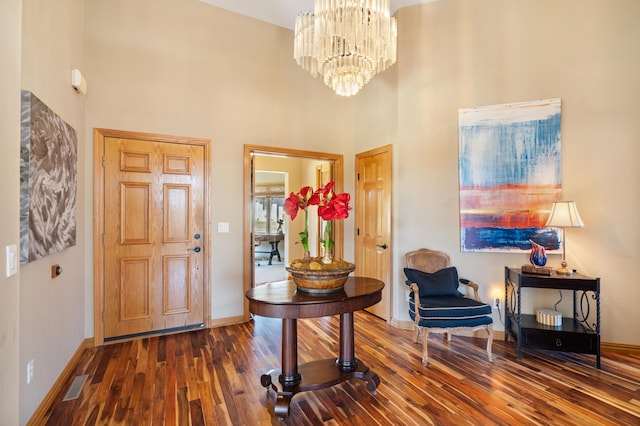 foyer entrance featuring wood finished floors, visible vents, baseboards, a high ceiling, and a notable chandelier