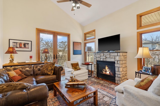 living area featuring a stone fireplace, ceiling fan, french doors, and high vaulted ceiling