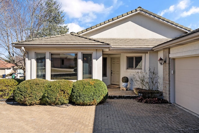 property entrance featuring a tiled roof, an attached garage, and stucco siding