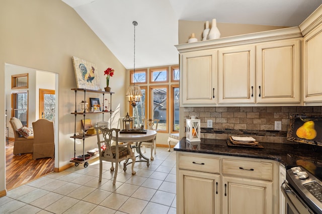 kitchen featuring light tile patterned floors, dark stone counters, stainless steel range with electric cooktop, decorative backsplash, and cream cabinets