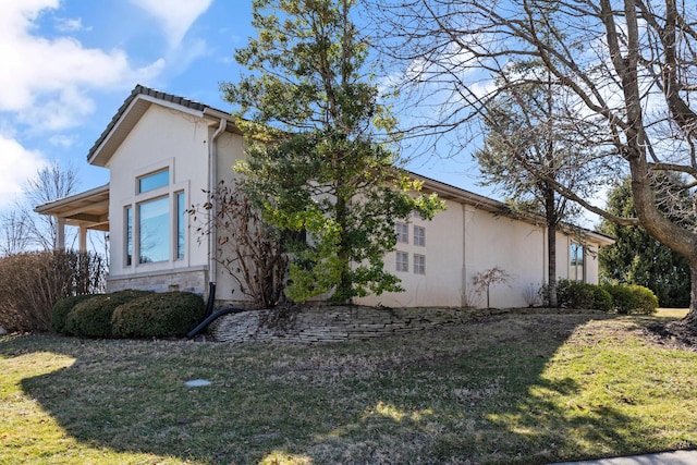 view of side of home featuring stone siding, a lawn, and stucco siding