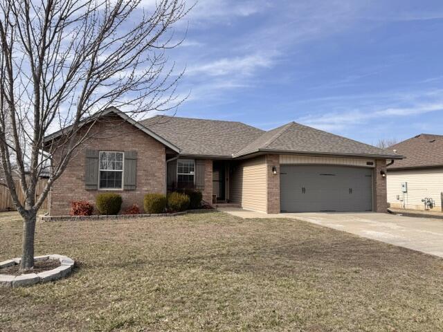 single story home featuring brick siding, a shingled roof, a front lawn, concrete driveway, and an attached garage