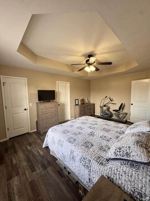 bedroom featuring dark wood-style floors, ceiling fan, baseboards, and a tray ceiling