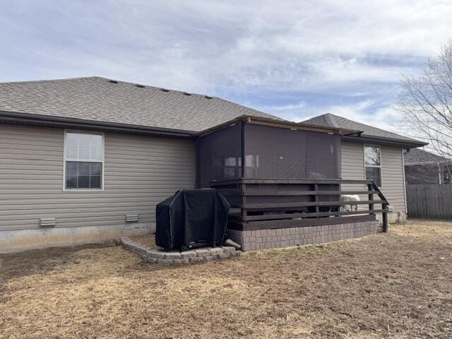 rear view of property featuring a sunroom, fence, and roof with shingles