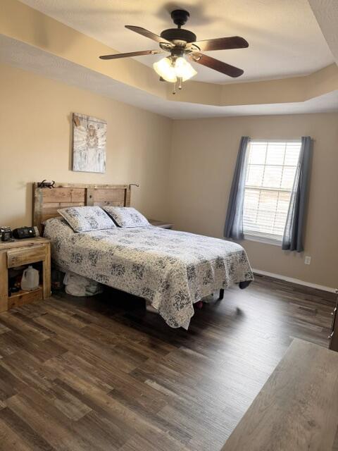 bedroom featuring a ceiling fan, a raised ceiling, wood finished floors, and baseboards