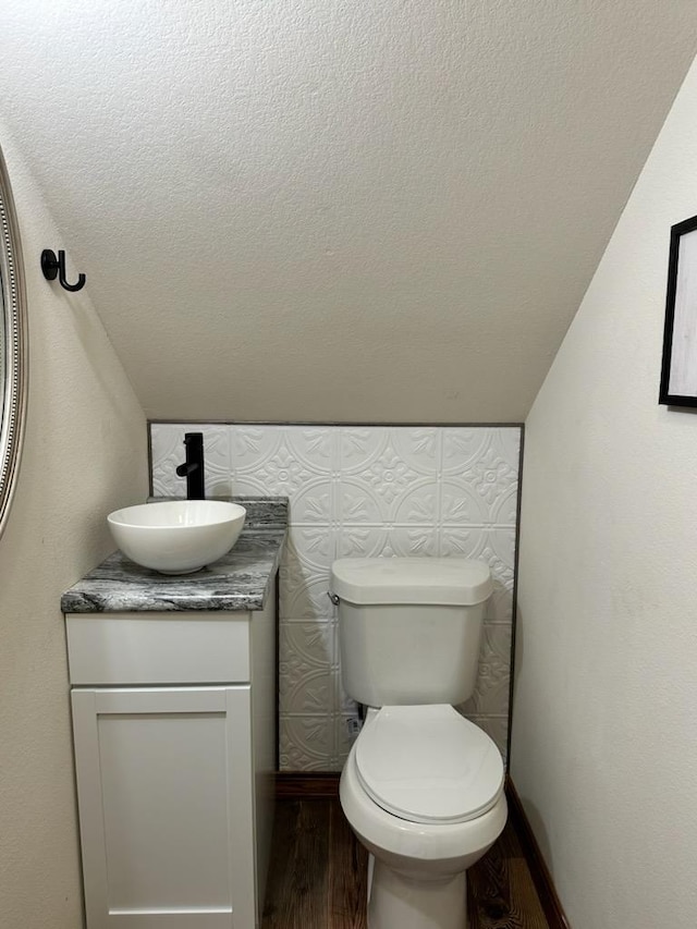 half bath with baseboards, toilet, vanity, wood finished floors, and a textured ceiling