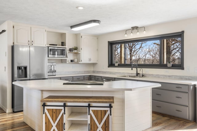 kitchen featuring a sink, gray cabinetry, a breakfast bar, appliances with stainless steel finishes, and open shelves