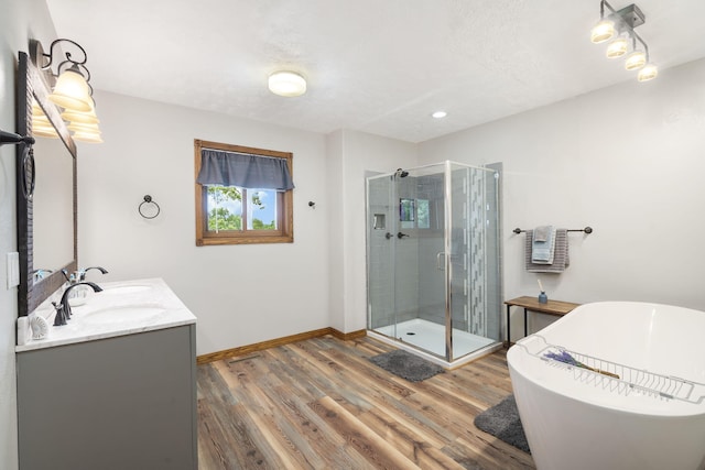 full bathroom with a freestanding bath, double vanity, a stall shower, wood finished floors, and a sink