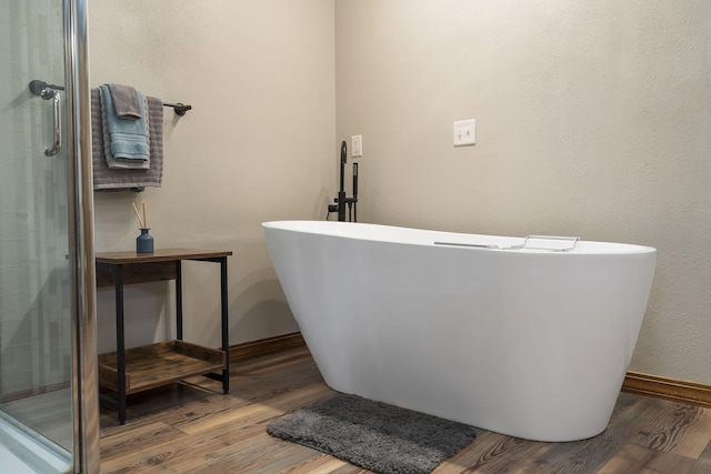 bathroom with a shower stall, a freestanding bath, baseboards, and wood finished floors