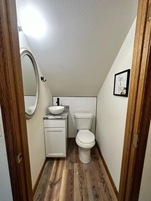 half bath with vanity, wood finished floors, vaulted ceiling, a textured ceiling, and toilet