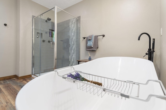 full bathroom featuring a shower stall, a freestanding tub, baseboards, and wood finished floors