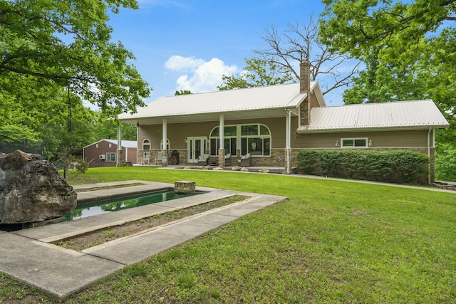 rear view of house with a yard, an outdoor pool, a chimney, and metal roof