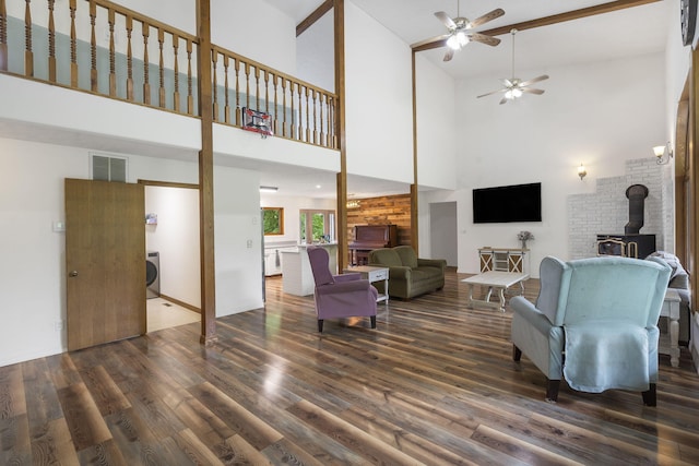 living area featuring visible vents, washer / clothes dryer, wood finished floors, a towering ceiling, and a wood stove