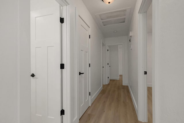 hall with light wood-style flooring, attic access, and baseboards