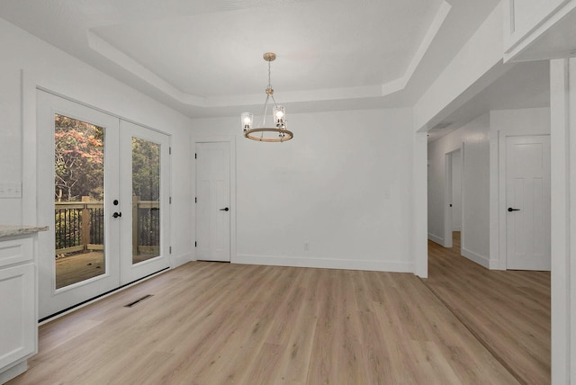 spare room featuring visible vents, baseboards, light wood-style flooring, french doors, and a raised ceiling