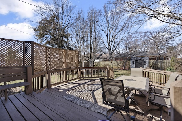 wooden deck with a fenced backyard, a storage unit, outdoor dining area, and an outdoor structure