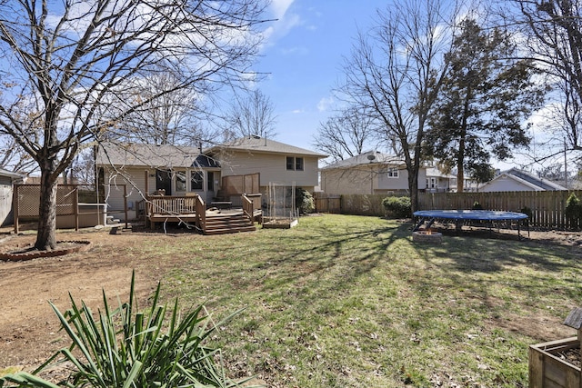 rear view of property featuring a yard, a deck, a trampoline, and a fenced backyard