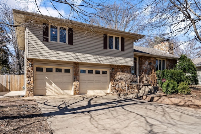 split level home with stone siding, a chimney, driveway, and fence