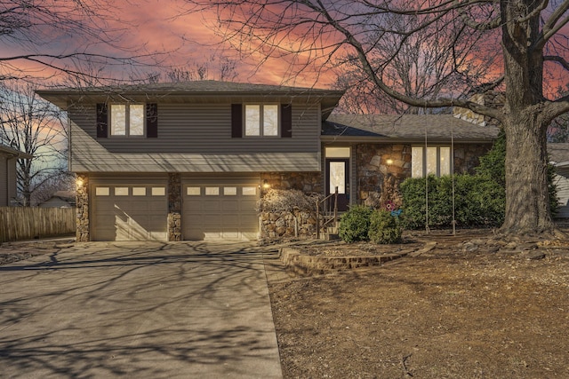 split level home with stone siding, an attached garage, concrete driveway, and fence