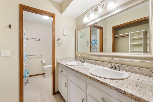 bathroom featuring double vanity, toilet, baseboards, and a sink