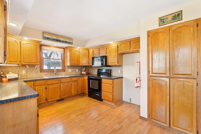 kitchen featuring black appliances, a sink, dark countertops, backsplash, and light wood finished floors