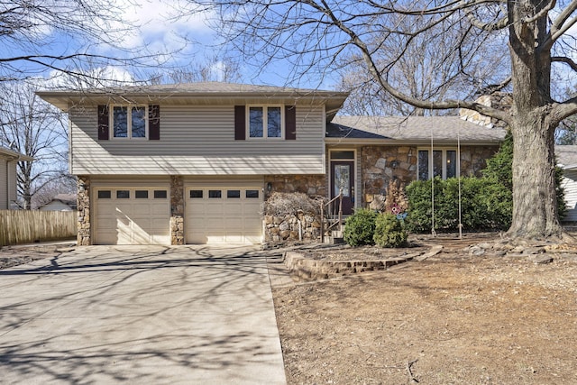 tri-level home with stone siding, an attached garage, driveway, and fence