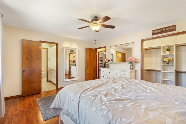 bedroom featuring baseboards, ensuite bath, wood finished floors, and a ceiling fan