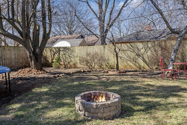 view of yard with a trampoline, a fenced backyard, and an outdoor fire pit