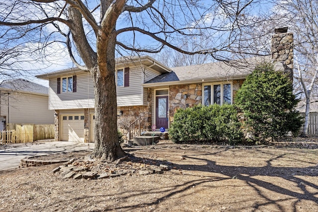 tri-level home featuring a chimney, stone siding, concrete driveway, and a garage