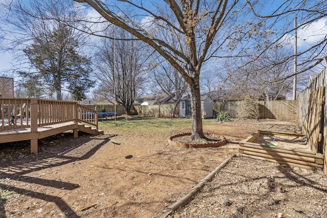 view of yard featuring an outbuilding, a fenced backyard, a wooden deck, and a trampoline