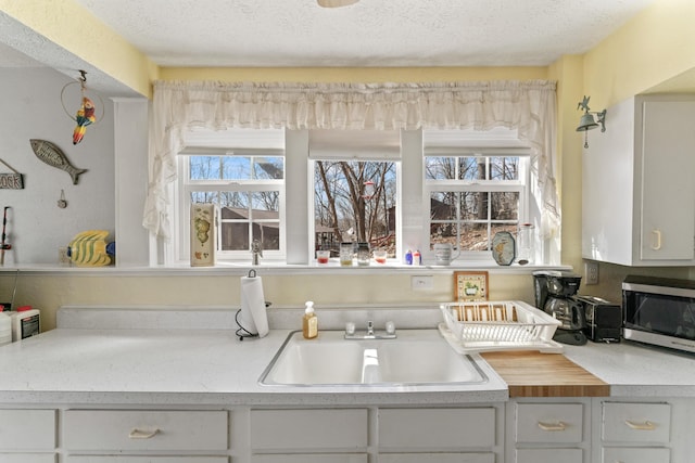 kitchen with white cabinets, a textured ceiling, light countertops, and a sink