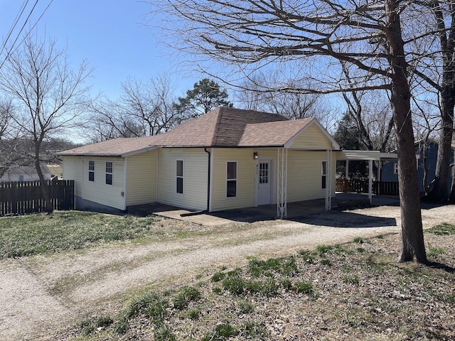 view of property exterior featuring a carport, roof with shingles, driveway, and fence