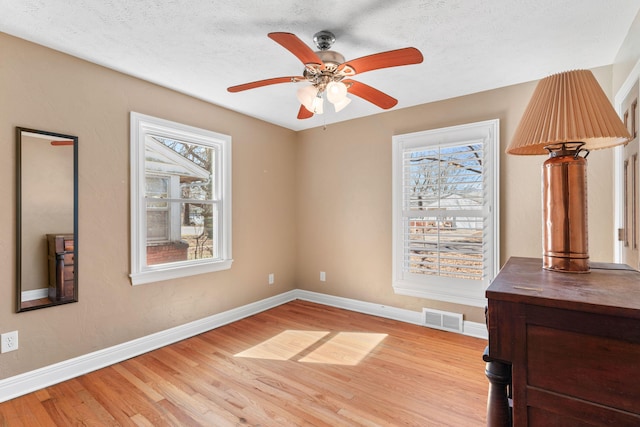 empty room featuring visible vents, ceiling fan, baseboards, light wood-style floors, and a textured ceiling