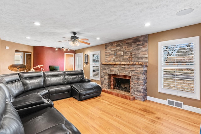 living room with wood finished floors, baseboards, visible vents, a stone fireplace, and a textured ceiling