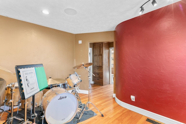 rec room with visible vents, rail lighting, wood finished floors, and baseboards