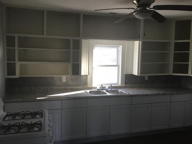 kitchen with white range with gas cooktop, open shelves, a sink, dark countertops, and ceiling fan