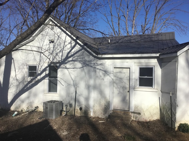 view of property exterior featuring central air condition unit, stucco siding, and metal roof