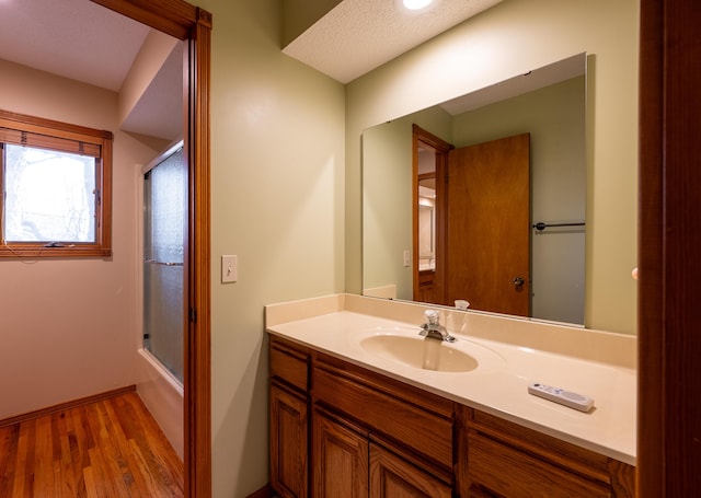 bathroom with combined bath / shower with glass door, baseboards, wood finished floors, and vanity