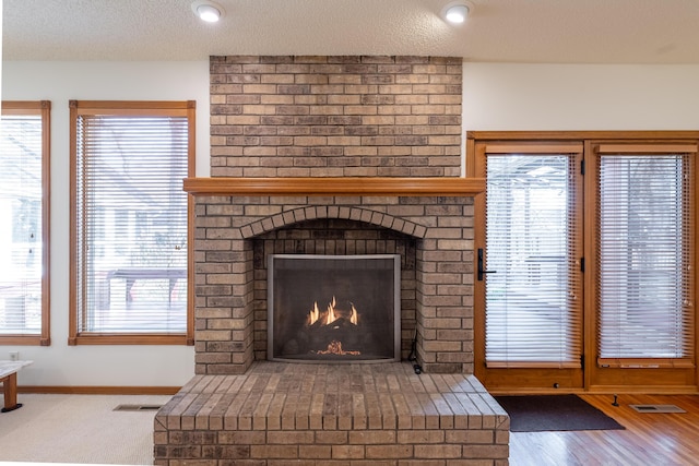 details with visible vents, a brick fireplace, a textured ceiling, and baseboards