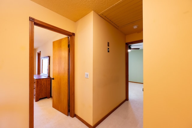 hall with a textured ceiling, baseboards, and light carpet