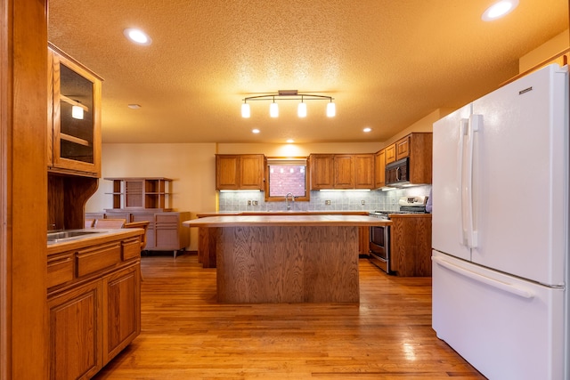 kitchen featuring freestanding refrigerator, brown cabinetry, light wood finished floors, black microwave, and stainless steel range with gas stovetop