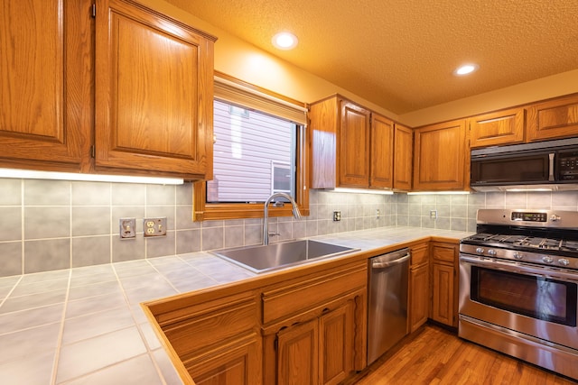 kitchen featuring a sink, tile countertops, brown cabinetry, and stainless steel appliances