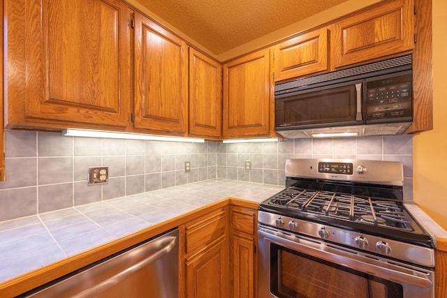 kitchen featuring tile countertops, stainless steel appliances, brown cabinets, and decorative backsplash