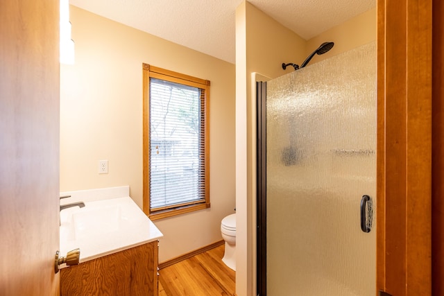 bathroom featuring toilet, a textured ceiling, wood finished floors, a shower stall, and vanity