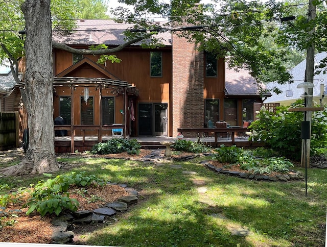 back of property with a shingled roof, a deck, a lawn, and a chimney